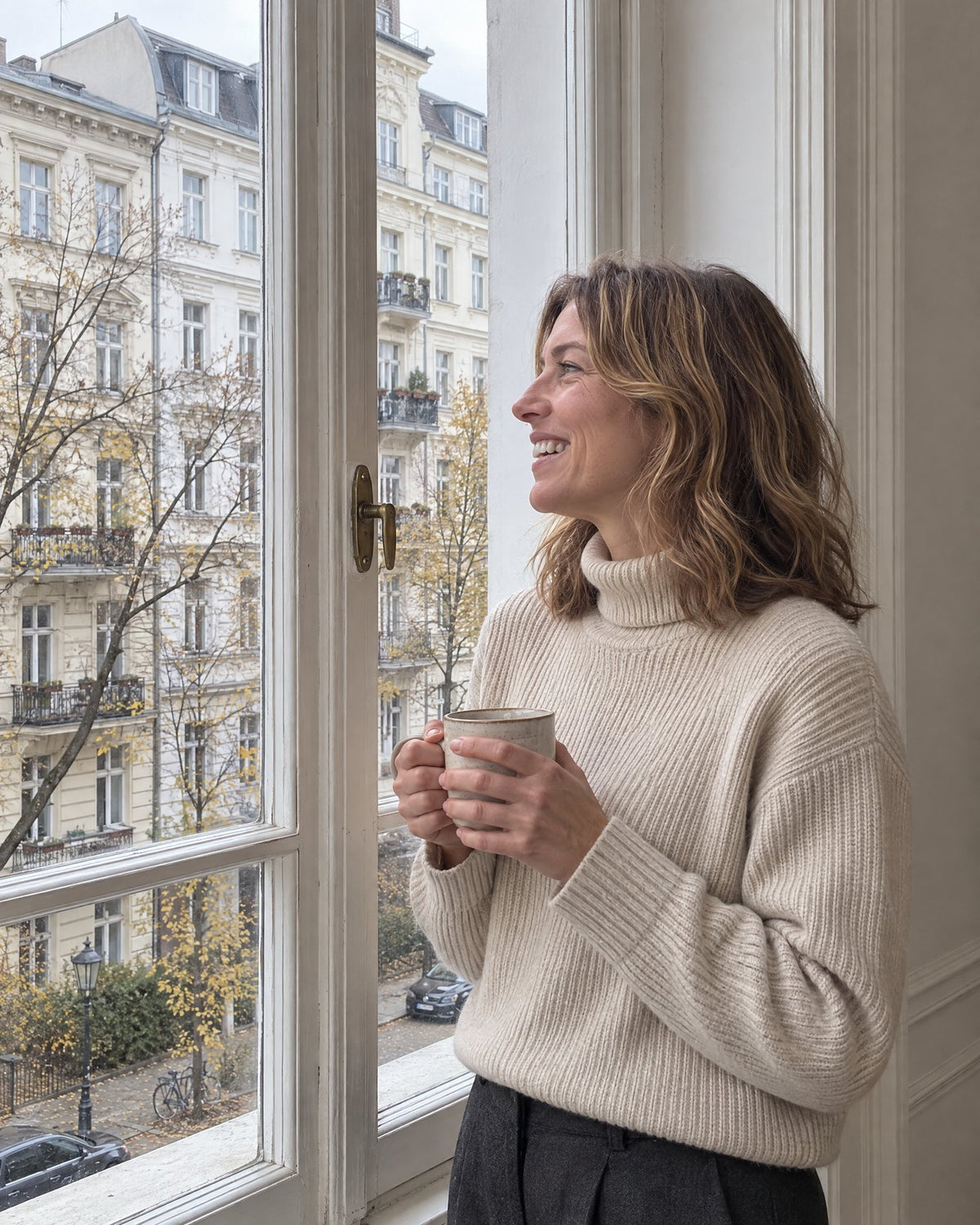 Frau im Rippstrick-Rollkragenpullover mit Tasse an einem hohen Altbaufenster